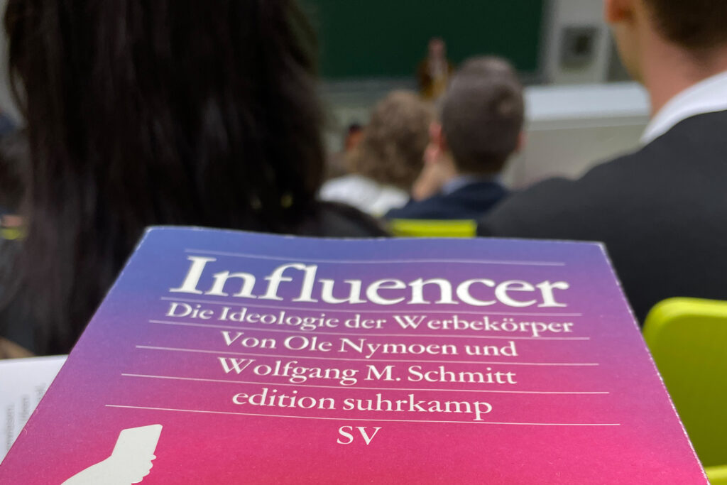 Das Buchcover von "Influencer - Die Ideologie der Werbeköper von Ole Nymoen und Wolfgang M. Schmitt (2021) im Hörsaal 3 des Campus-Center der Universität Kassel 