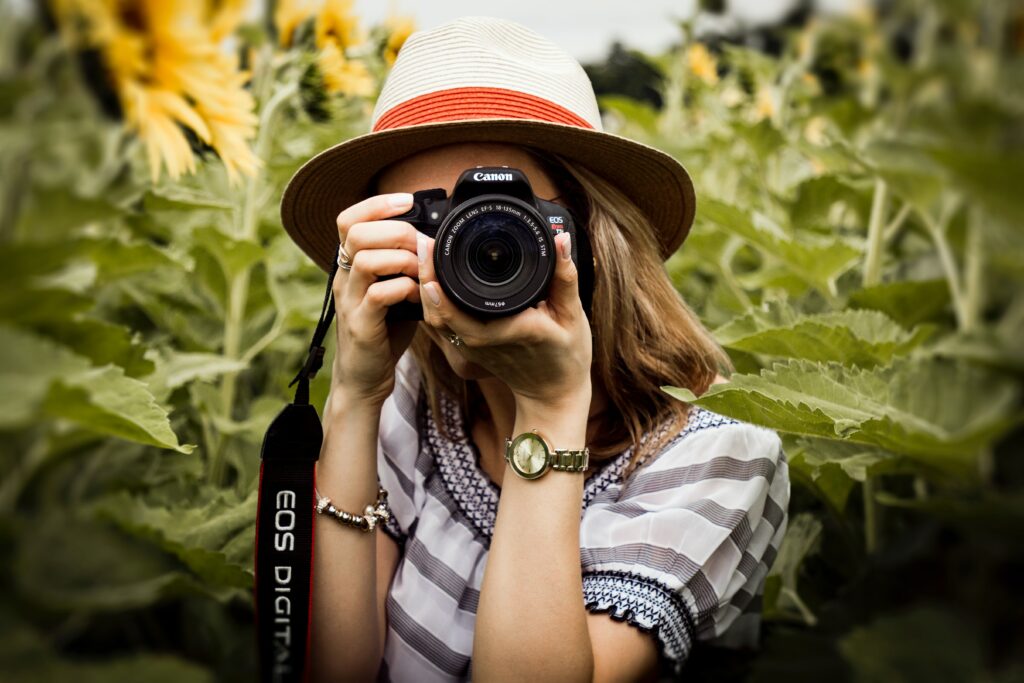 Die ideale Kamera für (arme) Journalisten – und solche, die keine Lust auf Backsteine in der Kameratasche haben 2 Eine Frau mit Hut hält eine Canon-Spiegelreflexkamera in den Händen. (Foto: Andre Furtado/pexels.com)